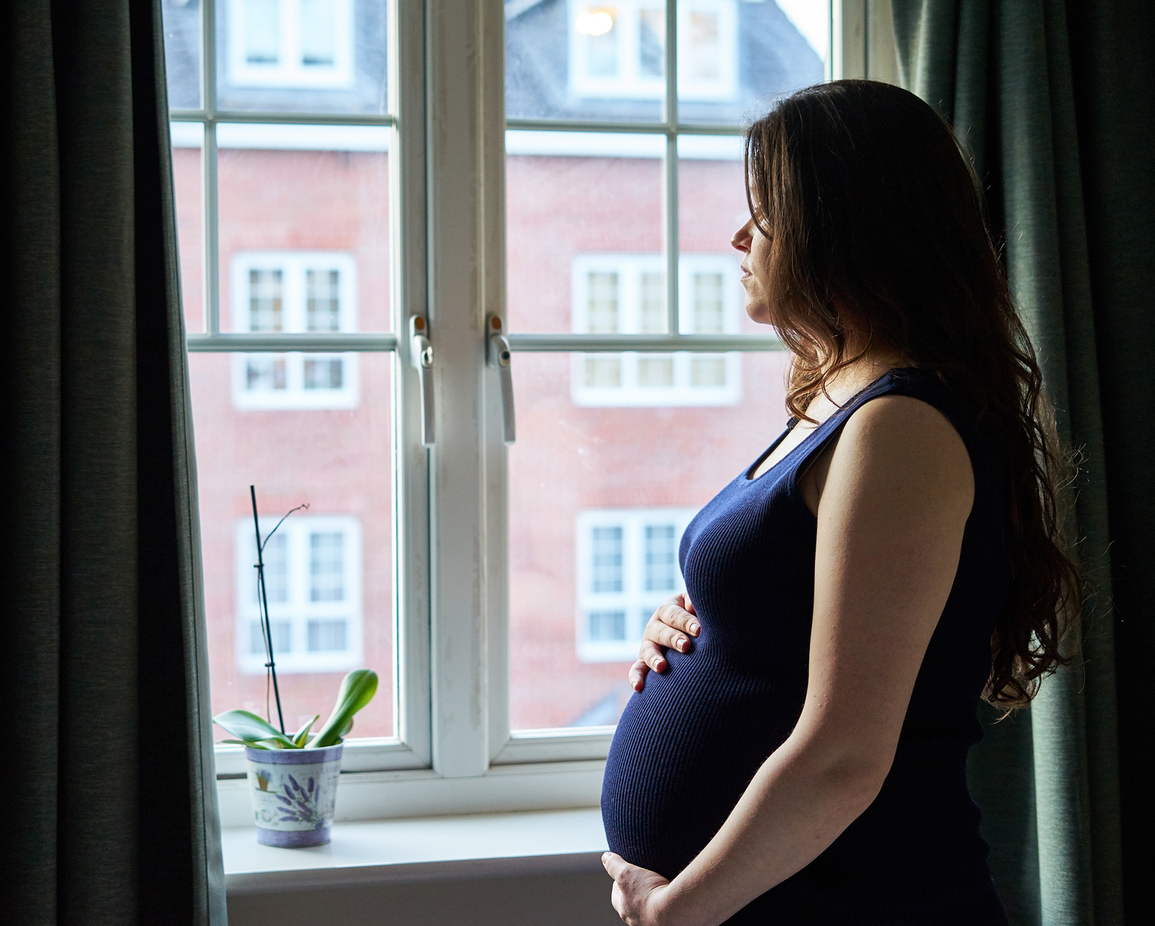 Pregnant woman looking out of window holding baby bump